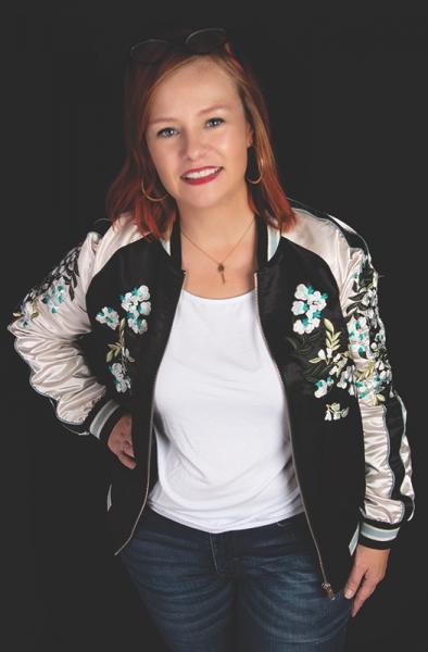 A woman with red hair wearing a silk floral bomber jacket.