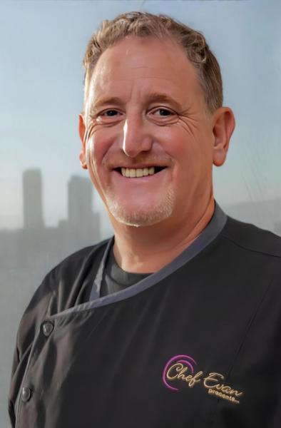 A smiling man wearing a black chef's jacket. He has reddish hair and a goatee.