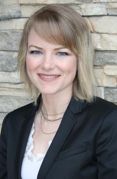 A blonde woman, leaning against a stone wall and smiling.