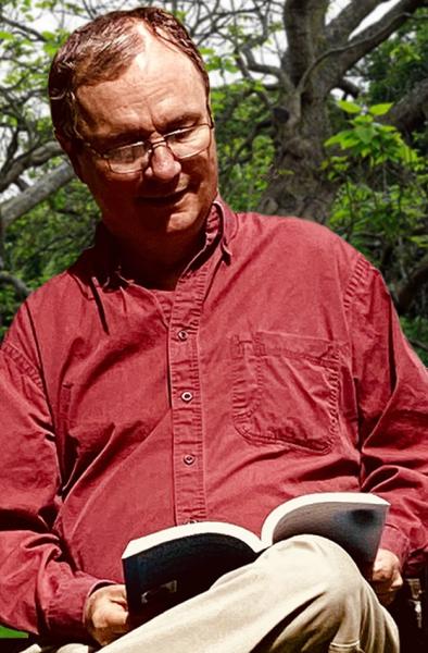 A photo of a man sitting on a bench, reading a book.