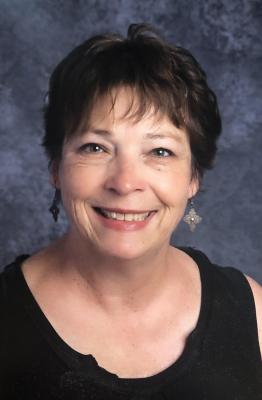 A smiling woman with short brown hair. She is wearing a black top with a U-shaped neck and no sleeves.